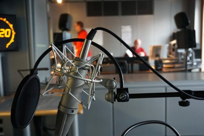 NDR Aufnahmestudio © Simon Brunke Ansicht eines Mikrofons, Personen im Hintergrund.