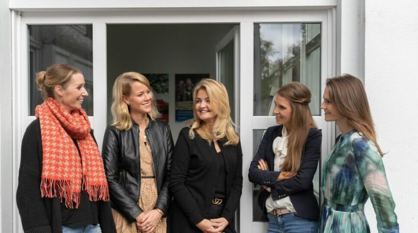 Fotografie von fuenf Frauen vor eine geoeffneten Glastuer draußen.