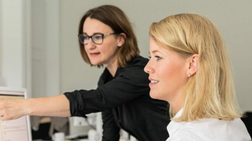 Zwei Frauen schauen auf einen Computerbildschirm.