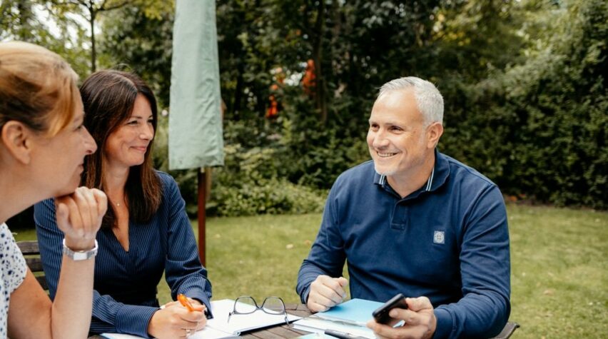 Fotografie einer Unterhaltung im Garten am Tisch mit Unterlagen.