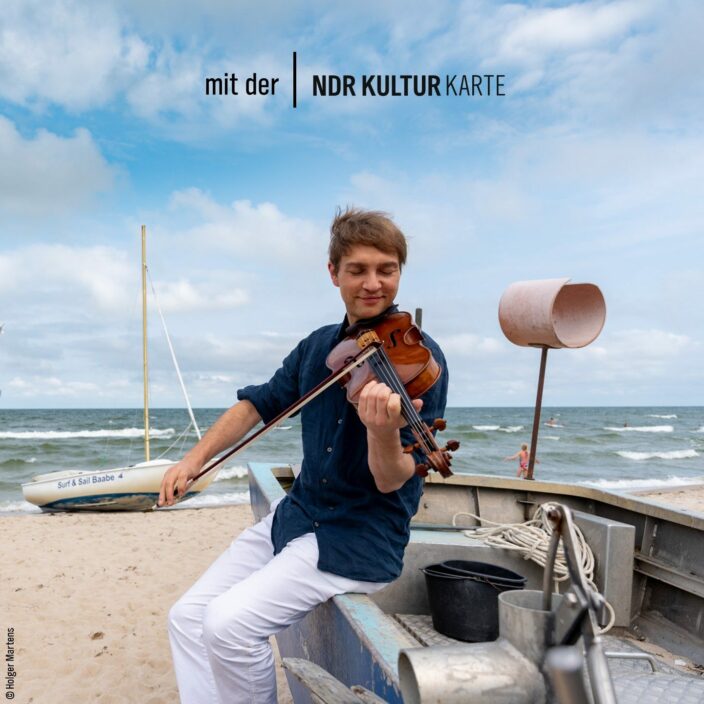 Festspiele Mecklenburg-Vorpommern © Holger Martens Musiker sitzt Bratsche spielend auf einem Boot am Strand.