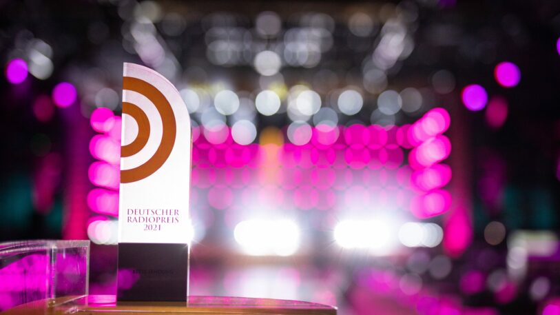 Die Auszeichnung Deutscher Radiopreis vor pinkem Hintergrund.