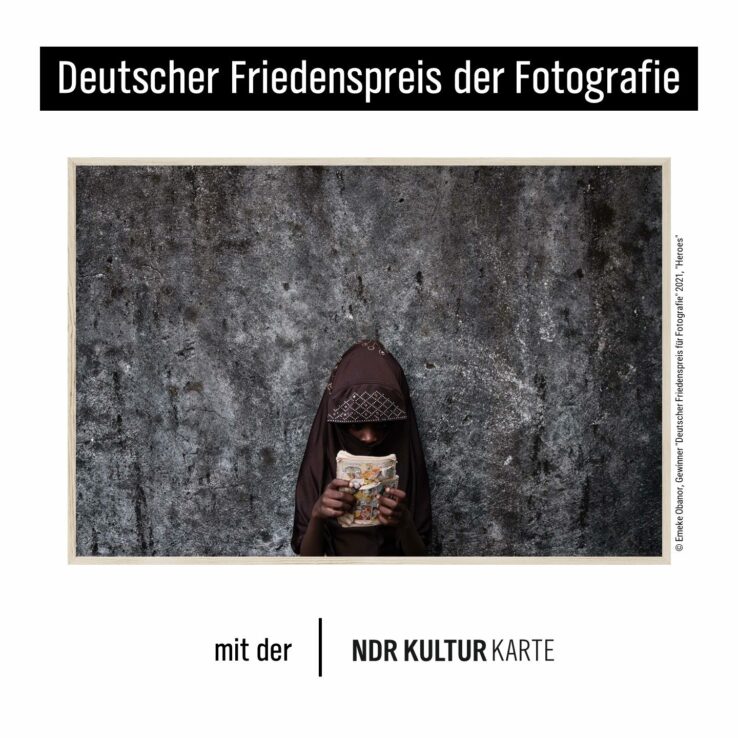 Ein Kind mit einem Comic steht vor einer grauen Wand.